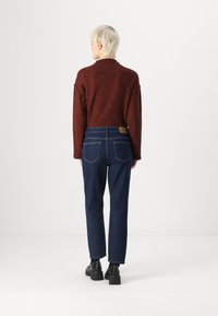 Sarkans teksturēts džemperis ar augstu apkakli, apvienots ar tumši ziliem sašaurinātiem džinsiem ar aizmugurējām kabatām un brendēta ādas etiķeti. Melni papēžu apavi.