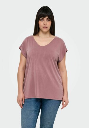 Haut à col en V et manches courtes en tissu doux couleur rose poussiéreux. Coupe décontractée avec une texture lisse. Associé à un jean bleu.