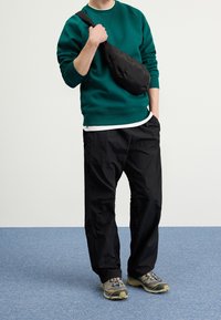 Sudadera de forro polar en teal, de corte relajado; pantalones de nylon negros; bolso de bandolera negro; zapatillas grises y beige con acentos coloridos.