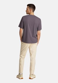 Gray short-sleeve t-shirt, smooth fabric, relaxed fit, worn with light beige pants and beige sneakers. Plain design, no visible patterns.