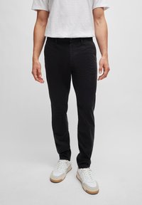 Czarne bawełniane spodnie o slim fit, z kieszeniami z przodu i zapięciem na guzik, w połączeniu z białymi sneakersami i jasnoszarym t-shirtem.