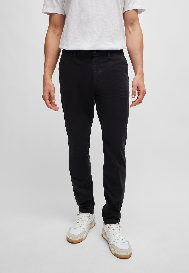 Czarne bawełniane spodnie o slim fit, z kieszeniami z przodu i zapięciem na guzik, w połączeniu z białymi sneakersami i jasnoszarym t-shirtem.