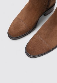 Botas de tobillo de ante marrón con un acabado suave, puntera redondeada y costuras decorativas a lo largo de la costura, que cuentan con un tacón bajo apilado.