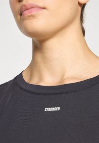 Sort sportstrøje med rund halsudskæring. Har hvid tekst "STRONGER" over kraven, glat tekstur og tætsiddende design.