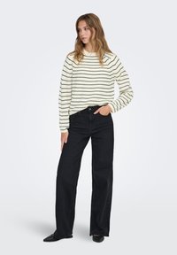 Pull en maille rayé crème et noir à coupe décontractée, associé à un jean noir taille haute à jambes droites et des ballerines pointues noires.