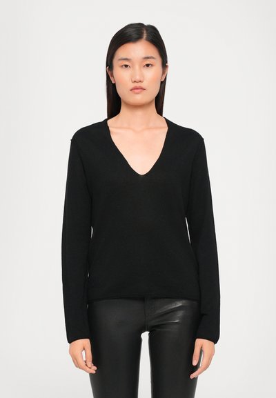 Black V-neck sweater in a soft knit material with long sleeves and a relaxed fit, paired with shiny black fitted pants.