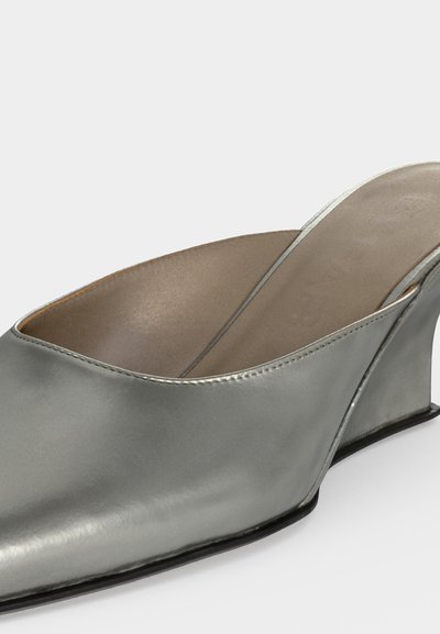 Mule argentée à enfiler avec talon compensé de hauteur moyenne et bout carré, présentant une tige en cuir lisse et une doublure intérieure beige.