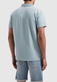 Lichtblauwe polo met korte mouwen, een klassieke kraag en een gladde textuur. In combinatie met lichte denim shorts, met opgerolde manchetten.