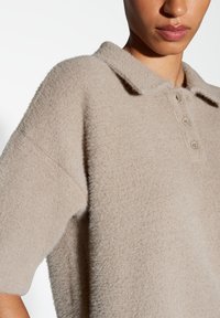 Polo beige à manches courtes avec une finition douce et texturée, doté d'un col et d'une patte de boutonnage à trois boutons.