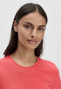 Korallinvärinen puuvillateeppari, jossa on pyöreä kaula-aukko, sileä pinta ja lyhyet hihat, mukautuvalla päällä ja siisteillä linjoilla.