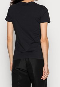 Czarna koszulka z krótkim rękawem i okrągłym dekoltem, wykonana z miękkiej bawełny. Widok z tyłu pokazuje dopasowany krój i gładką teksturę.