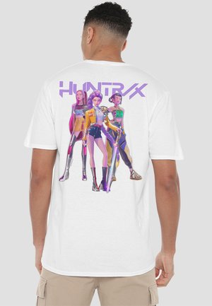 Weißes T-Shirt mit einem grafischen Druck von drei stilisierten Figuren in lebendigen Farben, mit dem Text "HUNTRAX" darüber.