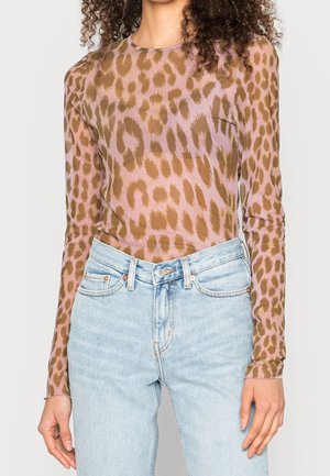 Femme portant un haut ajusté à manches longues avec un imprimé léopard rose et marron, associé à un jean taille haute bleu clair.