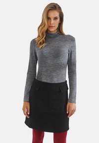 Szary długi rękaw golf połączony z czarną teksturowaną spódnicą z dwoma przednimi kieszeniami, noszony z czerwonymi legginsami.