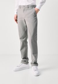 Light gray chinos made of cotton with a smooth texture, featuring a classic fit, side pockets, and worn with white sneakers.