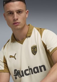 Puma Kurzarmtrikot in Creme mit goldenen Akzenten. Verfügt über einen Polo-Kragen, ein Vereinslogo und großen schwarzen "Auchan"-Text auf der Vorderseite.