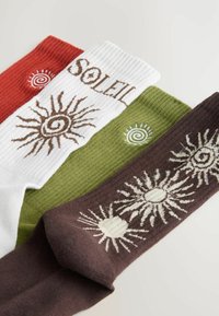 Tre par ribbede sokker i rød, hvid, grøn og brun. Hver sok har solmotiver, med "SOLEIL" broderet på den hvide sok.