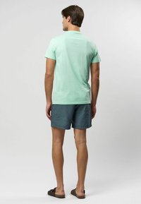 Mátově zelené tričko s krátkým rukávem, spárované s námořnickými modrými a bílými pruhovanými šortkami. Šortky mají elastický pas a volný střih.