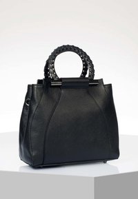 Sac à main en cuir noir avec surface texturée, poignées supérieures arrondies avec détails en forme de trous, et forme rectangulaire structurée sur un piédestal blanc.