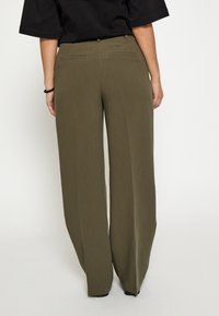 Olijfgroene broek met wijde pijpen en een textuur stof, met achterzakken en een aansluitende tailleband.