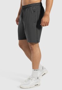Dunkelgraue Shorts mit elastischem Bund, verstellbarem Kordelzug, Seitentaschen und einem glatten, leichten Stoff. Getragen mit weißen Sneakers.