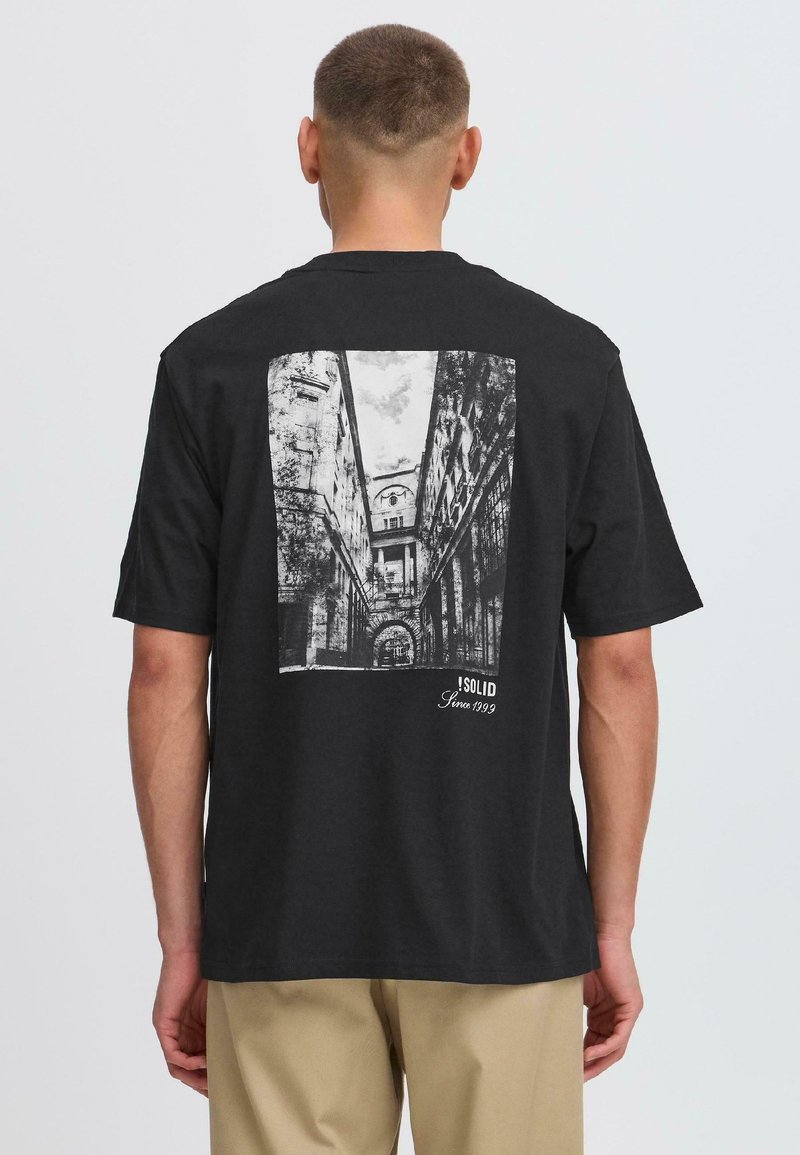 Camiseta negra de manga corta con un gran gráfico arquitectónico monocromático en la parte posterior, con el texto "SOLID Since 1999" en la esquina.