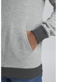 Gray sweatshirt with a kangaroo pocket, ribbed cuffs, and hem. Features a soft texture and a contrasting darker gray band at the bottom.