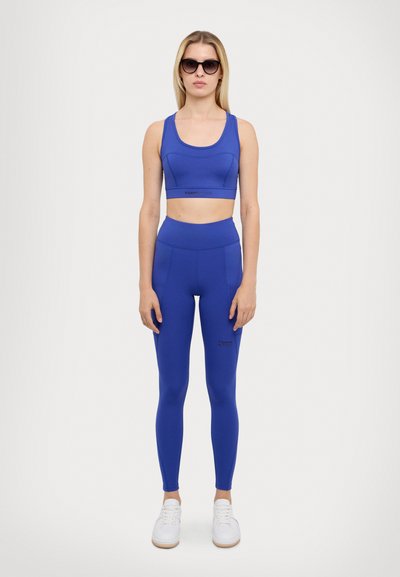 Blue sports bra and high-waisted leggings made of stretch fabric, featuring a smooth texture and fitted design. Accented with logo detail.