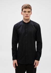 Fekete, hosszú ujjú ing, magas gallérral, sima anyagból készült. Gombos elülső plakkal és testhezálló szabással.