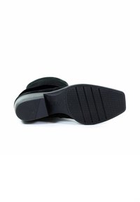 Zwarte suède enkellaars met een gestructureerde rubberen zool en een gladde, taps toelopende hak. De zool heeft verticale groeven voor grip.
