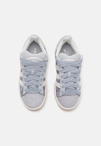 Ljusblå sneakers med ett texturerat mönster, tillverkade av mocka och textilmaterial. Inkluderar tre vita ränder och matchande snören.