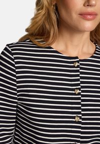 Haut rayé marine et blanc avec un col rond, doté de quatre boutons en forme de cœur dorés sur le devant. Matière en coton lisse.