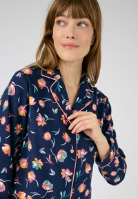 Camisa de pijama color azul marino con un patrón floral en rosa y amarillo, con cuello de muesca y botones en rosa. Textura de tela suave.