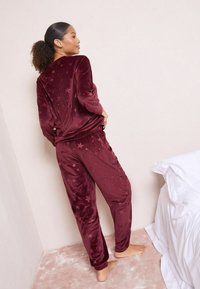 Set de loungewear din velur bordeaux cu mâneci lungi și talie elastică, având modele subtile cu stele și o textură moale și netedă.