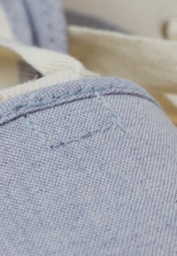 Lichtblauwe stoffen schoen close-up, met een textuur van canvas, contrasterende gestikte accenten en zichtbare stikdetails aan de bovenrand.