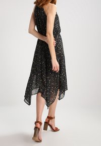 Czarna midi sukienka w kwiaty o zwiewnej, przejrzystej fakturze, z dekoltem w typie halter i asymetrycznym dołem. Posiada dopasowaną talię i warstwową tkaninę.