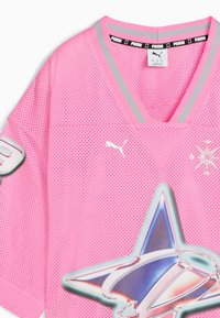 Roosa peenike võrgust spordijerseys, millel on hõbedased ja roosad triibud V-kaelas, Puma logo ja suur metalliksinine ning hõbedane tähis ees.