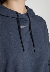 Sudadera de color azul oscuro con un tejido texturizado, cordones negros y un brillante logo plateado de Nike en el pecho.