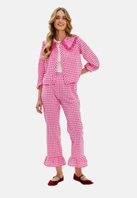 Růžový kostkovaný souprava obsahující límečkovou zkrácenou bundu s volánovými detaily a odpovídající kalhoty se rovnými nohavicemi a volánovými manžetami.