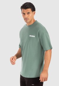 Grøn bomulds t-shirt med korte ærmer og rund hals, prydet med et hvidt "SMILODOX" logo på brystet. T-shirten har en afslappet pasform og en glat tekstur.