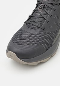 Gros plan d’une basket grise avec une tige en mesh texturé, des lacets assortis et une semelle beige avec un logo embossé sur le bout.