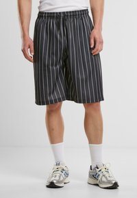 Shorts noirs avec des rayures verticales blanches, en tissu léger, dotés d'une taille élastique et de poches latérales.