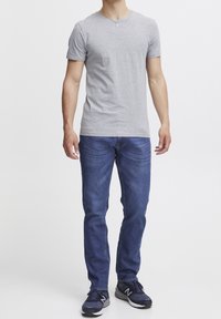 Grå kortärmad t-shirt, marinblå denimjeans och svarta sportskor. Passformen är avslappnad, med rund hals och klassisk femfickdesign.