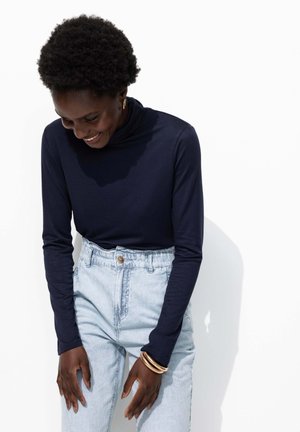 Un turtleneck à manches longues marine associé à un jean taille haute bleu clair. La tenue présente une texture lisse et un design minimaliste.