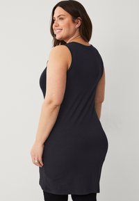 Zwart mouwloos jurkje met een getailleerd ontwerp, zachte stof en een gebogen zoom. Zichtbare stiksels en een ronde halslijn. Lange lengte tot halverwege de dij.