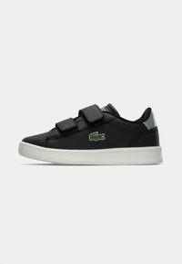 Scarpa in pelle nera con due cinturini in velcro, suola in gomma bianca e logo di coccodrillo verde discreto sul lato. Presenta un design a punta rotonda.