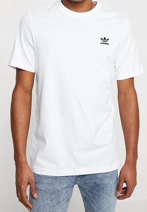 White cotton t-shirt with short sleeves, round neckline, and a black Adidas logo on the left chest. Worn with light blue jeans.