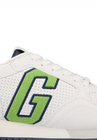 Weißer Sneaker mit einem perforierten Leder-Obermaterial, grünem Filz-Aufnäher "G", marineblauen Akzenten und weißen Schnüren auf einer hellen Sohle.