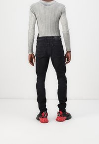 Vaqueros de mezclilla negros con un corte ajustado, combinados con una camiseta de manga larga gris con canalé. Zapatillas rojas y negras destacan en el conjunto.