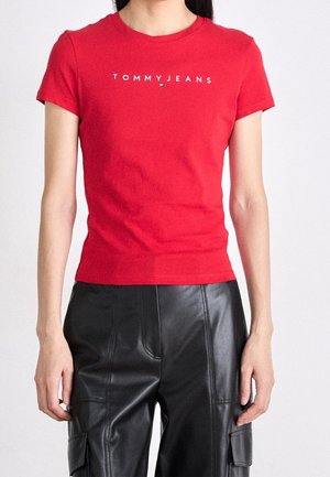 Czerwona bawełniana koszulka z krótkim rękawem, z białym logo "TOMMY JEANS" na przodzie. Noszona z czarnymi skórzanymi spodniami.